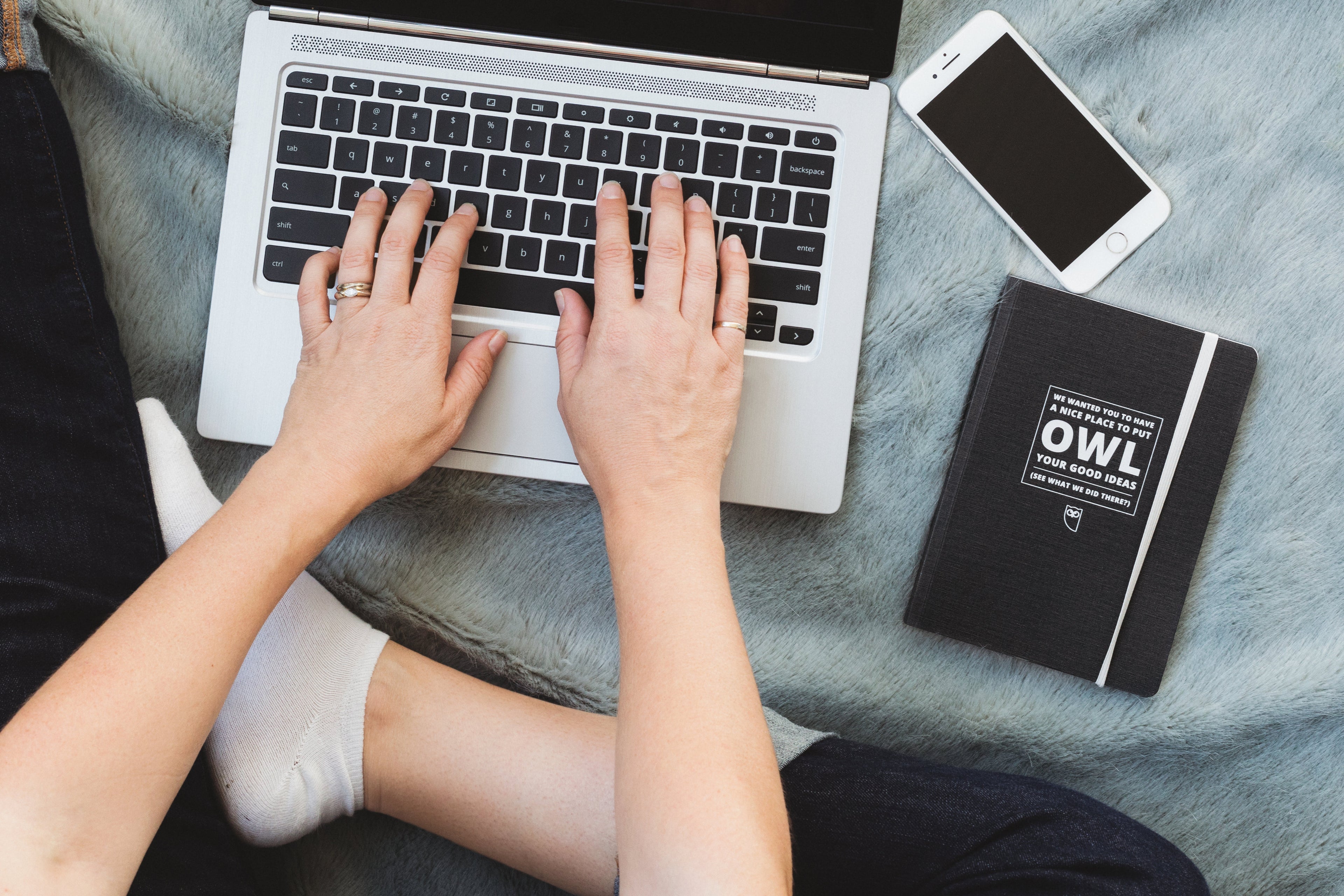Person working on laptop with phone and notebook beside